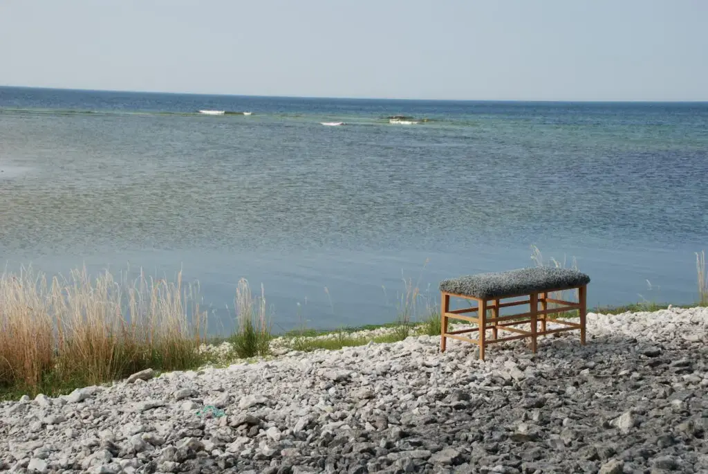 Bänk i ek med fårskinn av konstnär på strand på Gotland