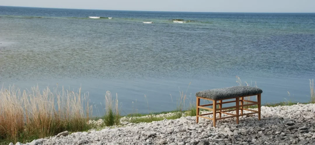 Bänk i ek med fårskinn av konstnär på strand på Gotland